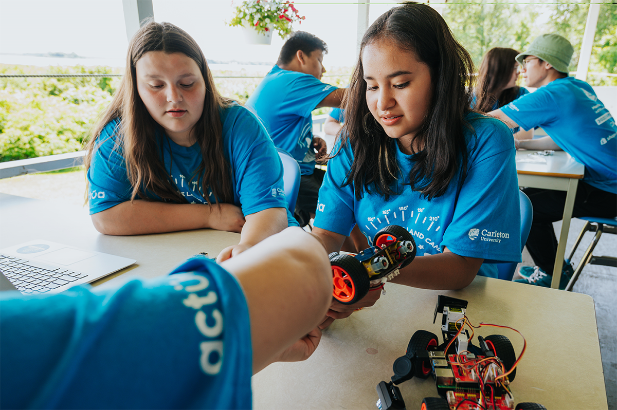 Young people wearing Actua t-shirts working together on a robotic AI-piloted car.