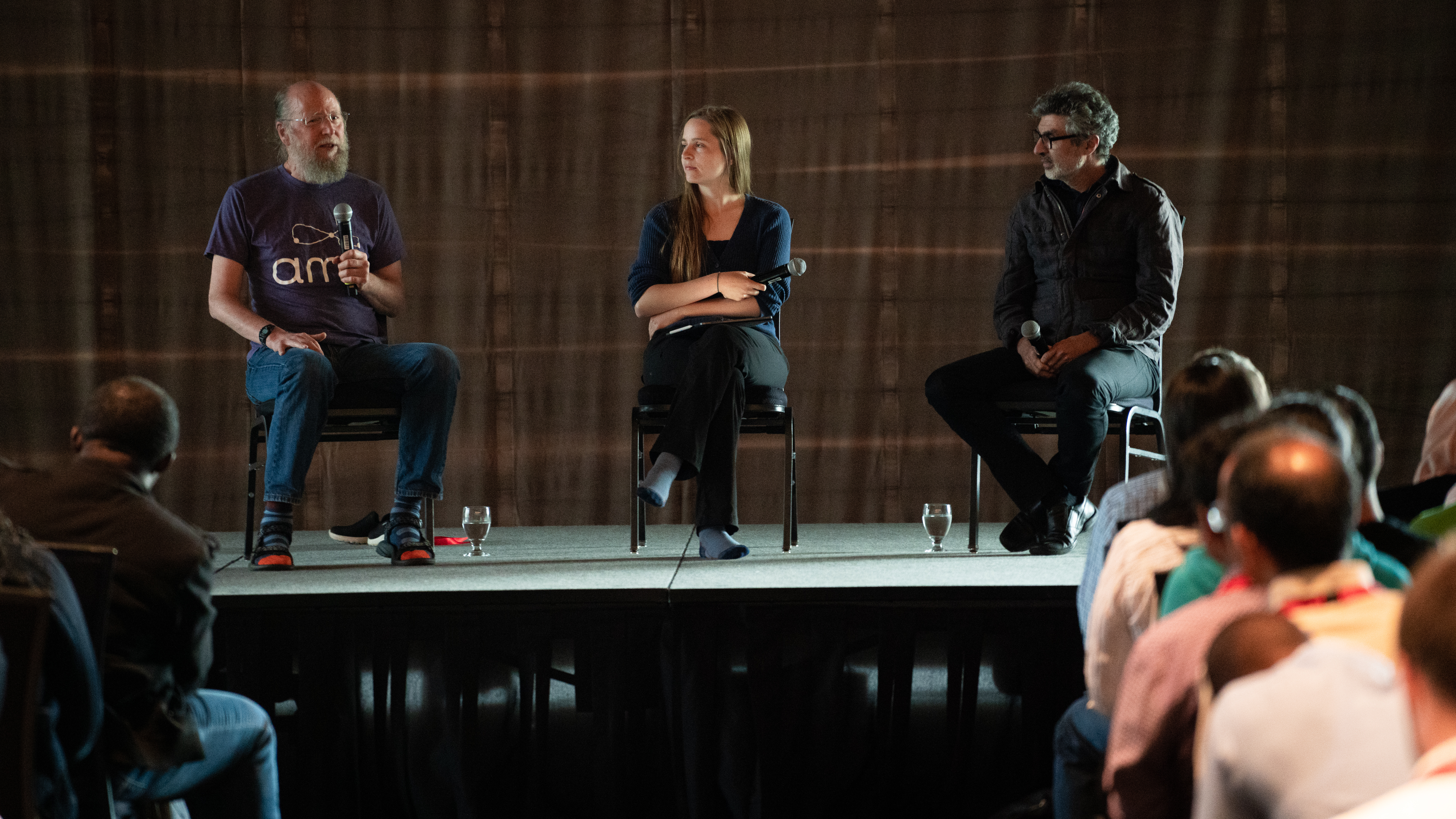 Three people sit on chairs on a stage