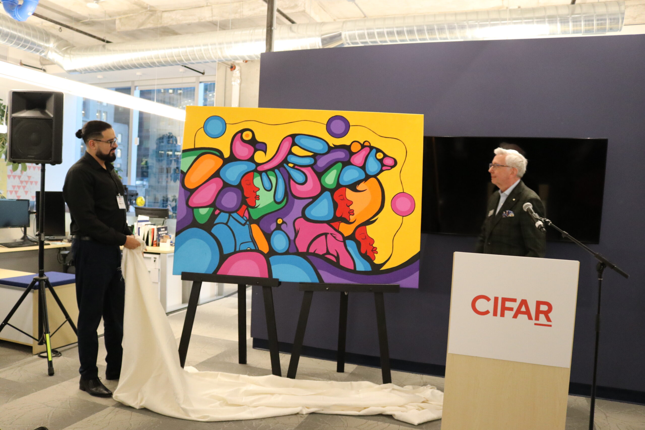A photo of Blake Angeconeb unveiling his new artwork which will be showcased in CIFAR’s Legacy Space. The theme of the artwork is "Two-Eyed Seeing" (Etuaptmumk), a concept that brings together Indigenous and Western ways of knowing. 